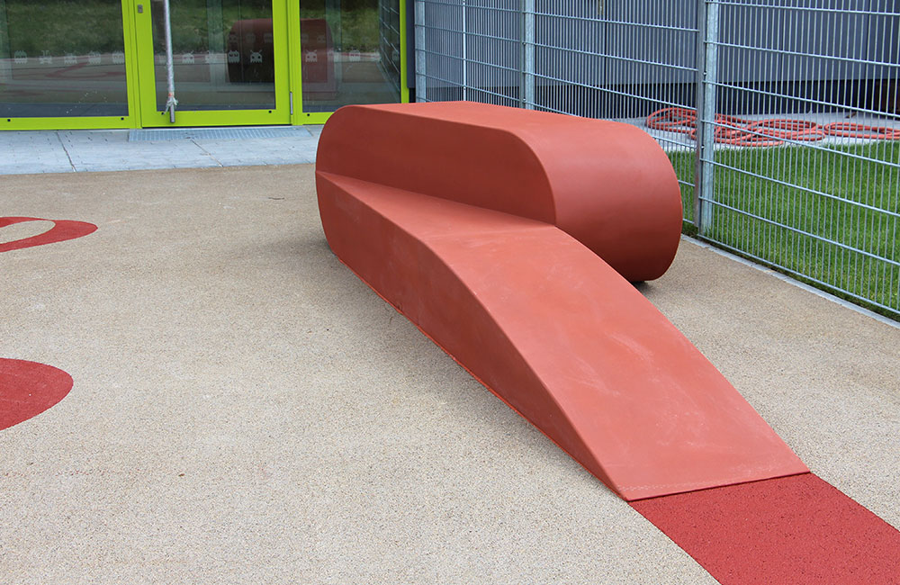 Eine künstlerisch gestaltete rote Sitzbank aus Glasfaserbeton ist Teil einer Aussenanlage der Arche in München Moosach
